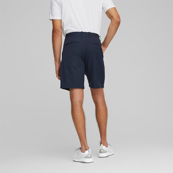 A model poses against grey, wearing a white t-shirt, navy shorts, and running shoes.